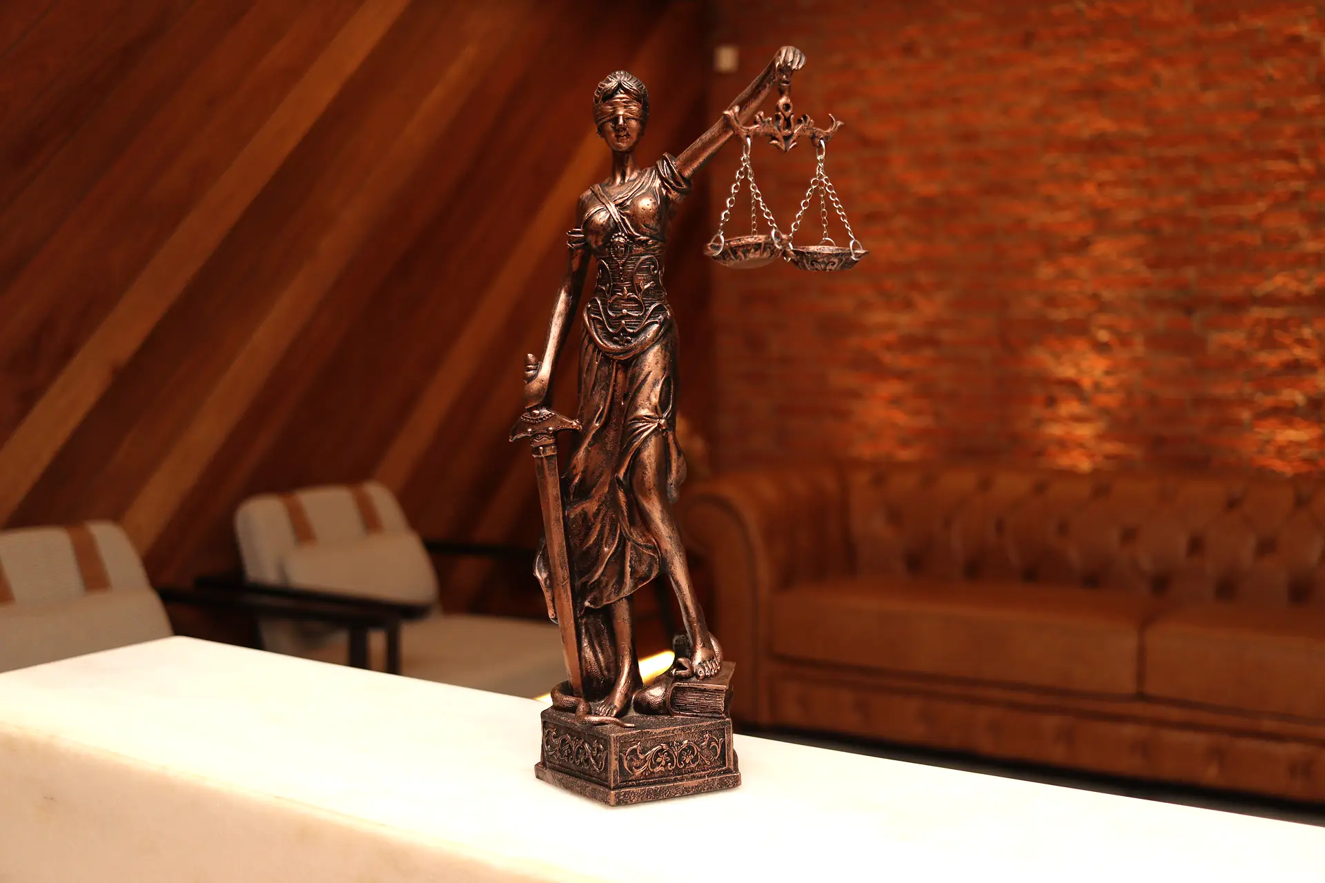 Estatueta de Têmis, deusa da Justiça, com balança e espada sobre balcão de mármore, com a sala de espera desfocada ao fundo