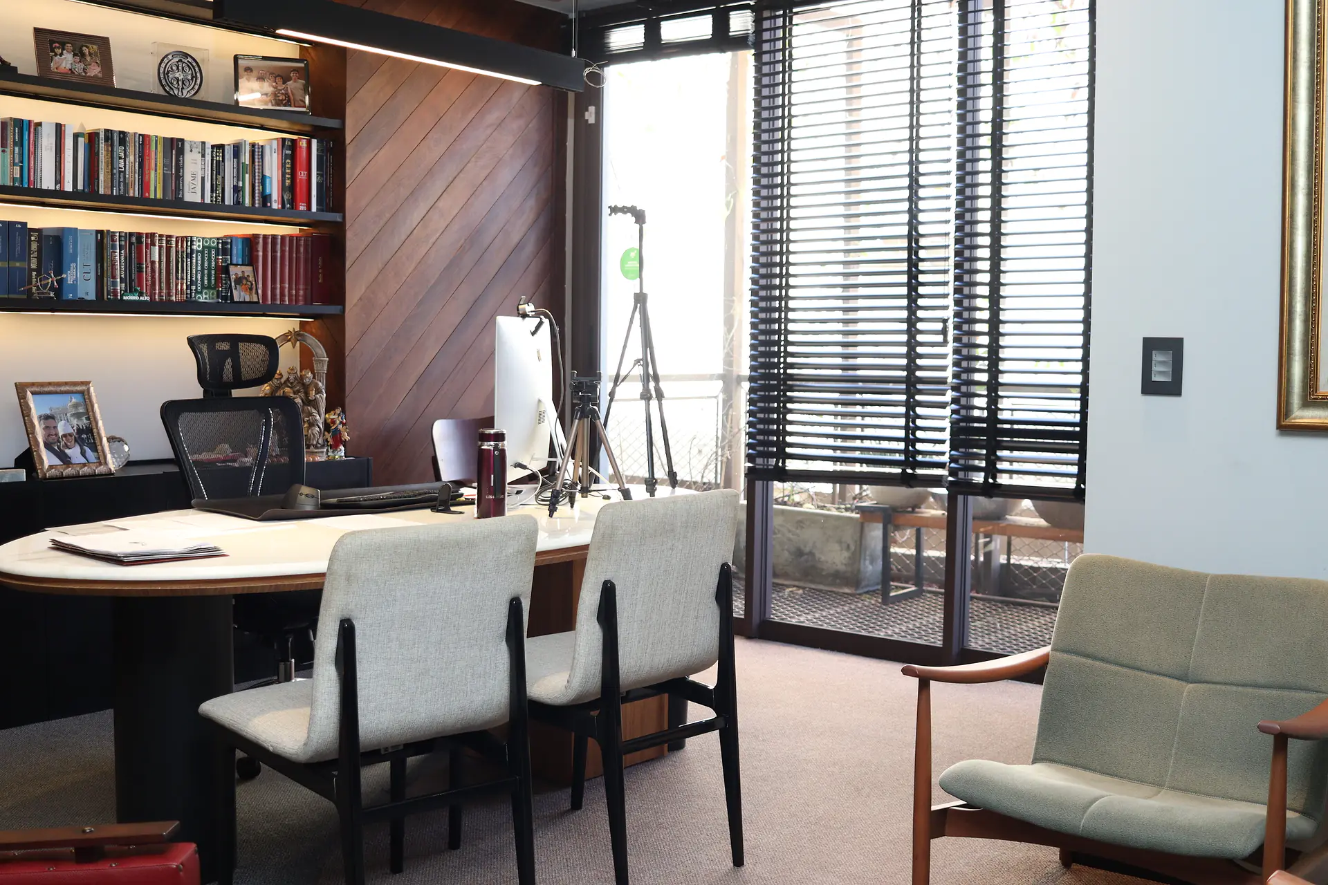 Sala de atendimento do sócio com mesa de mármore, cadeiras estofadas, estante de livros e porta de vidro para a varanda